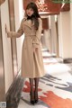 A woman in a beige trench coat leaning against a wall.